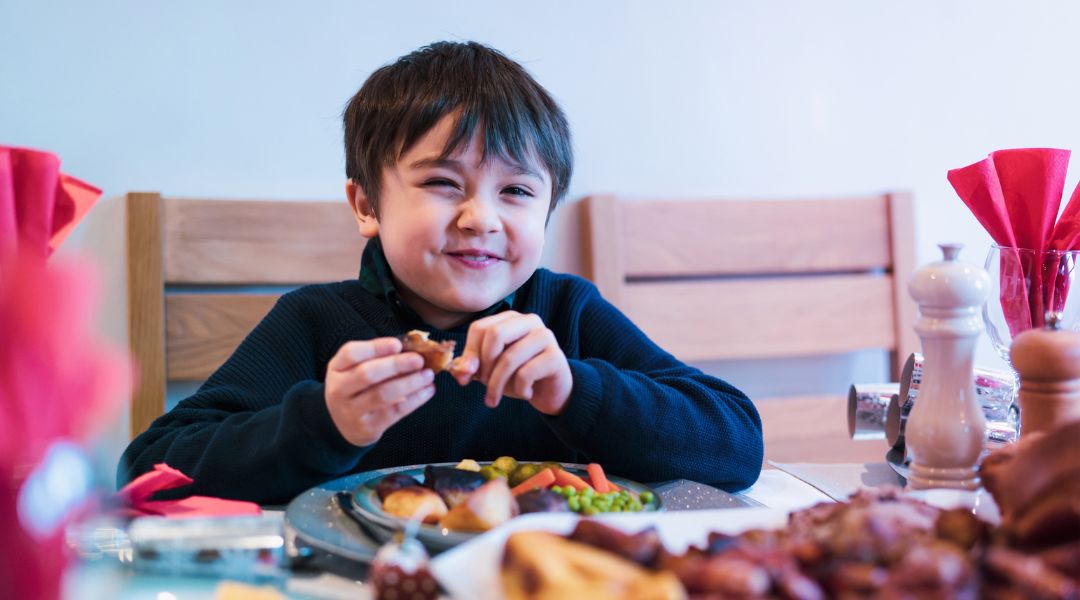 Garçon souriant dégustant un repas à une table, entouré de légumes et de plats rôtis