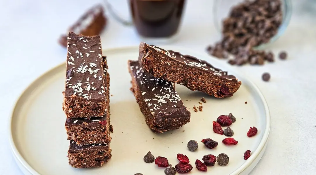 Barres protéinées au chocolat et canneberges séchées garnies de noix de coco râpée, servies sur une assiette