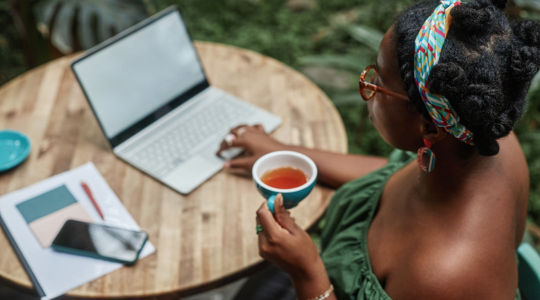 femme buvant une tasse de thé chaud tout en travaillant à l'extérieur à son ordinateur