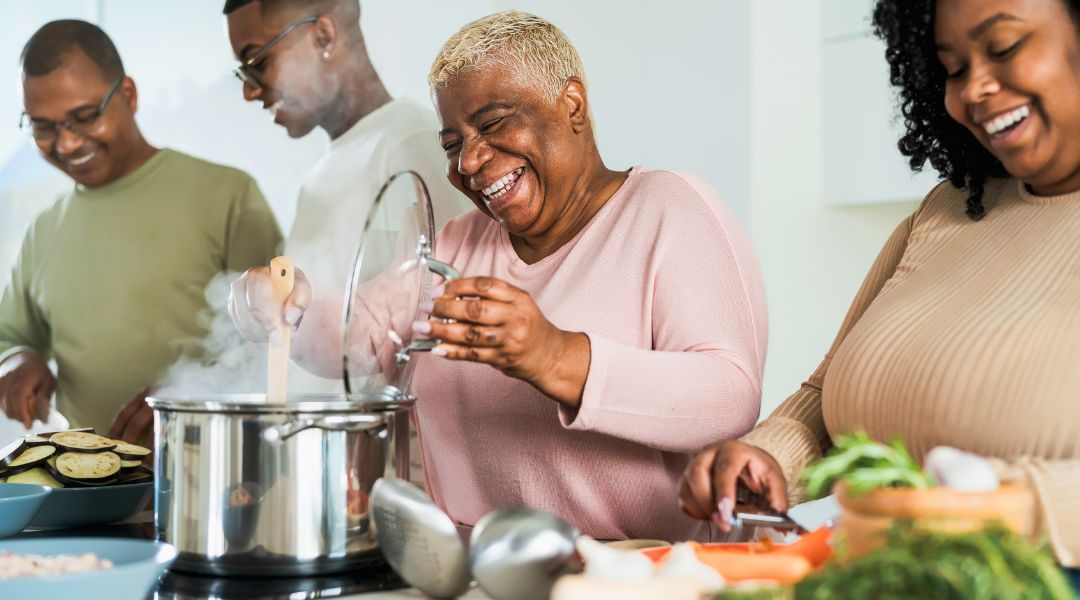 Groupe de quatre personnes riant et cuisinant ensemble dans une cuisine, préparant un repas avec des légumes frais