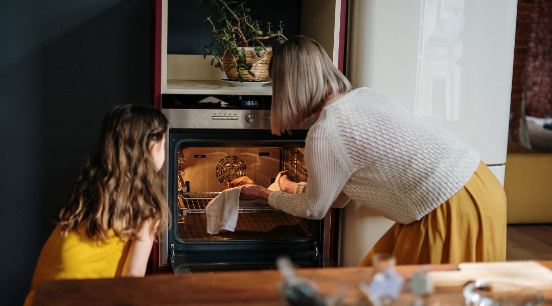 Femme et jeune fille cuisinant ensemble, plaçant un plat dans un four dans une cuisine chaleureuse