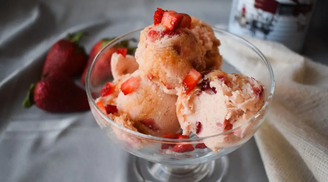 Crème glacée à la fraise maison servie dans une coupe, décorée de morceaux de fraises fraîches