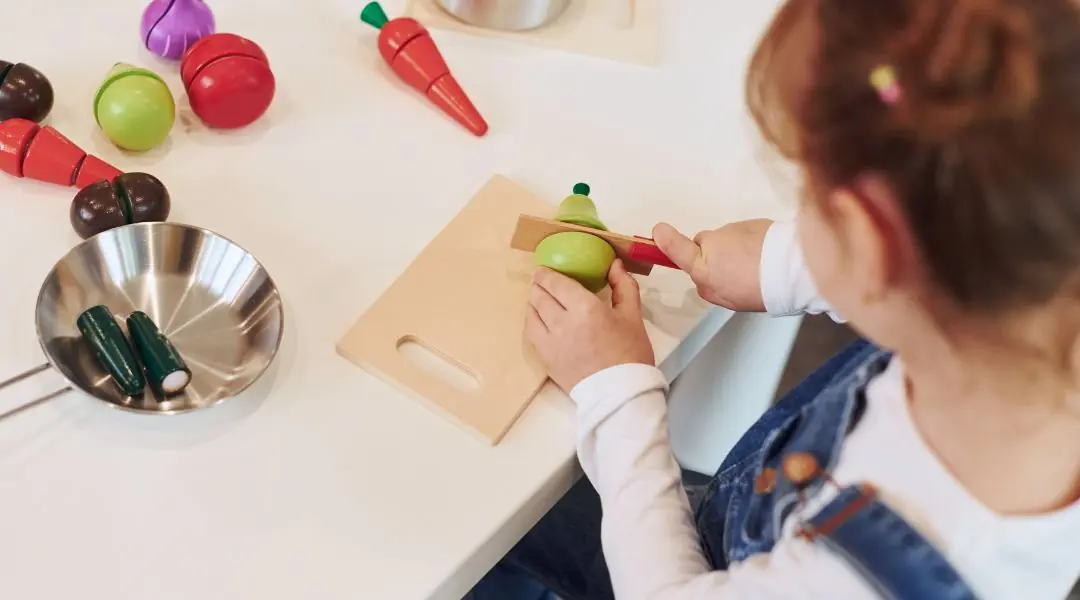Enfant jouant à couper des légumes en bois sur une planche