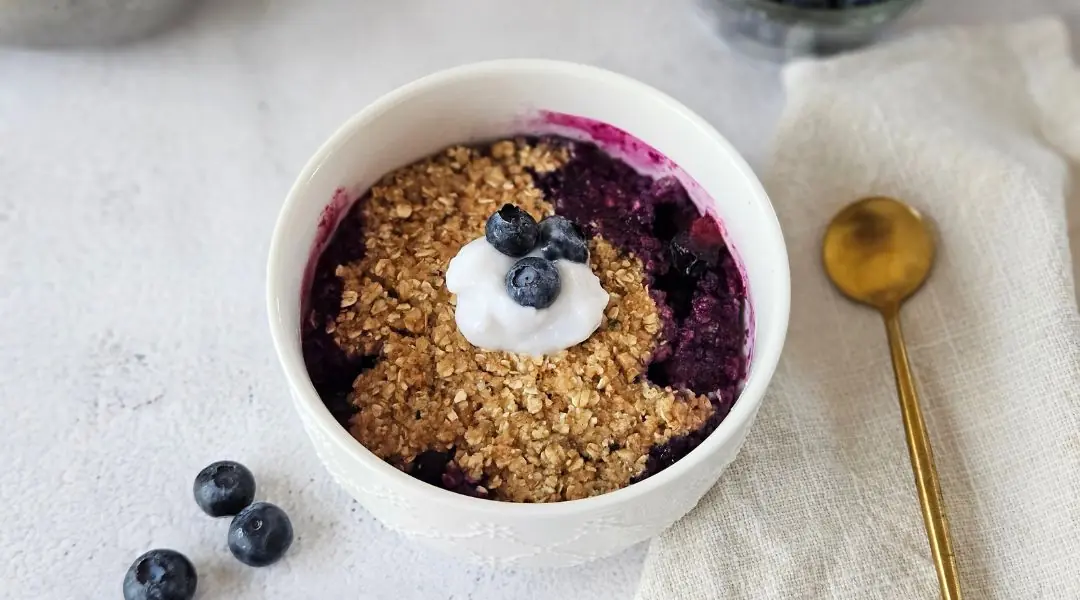 Crumble aux bleuets dans un bol blanc, garni de yogourt et fruits