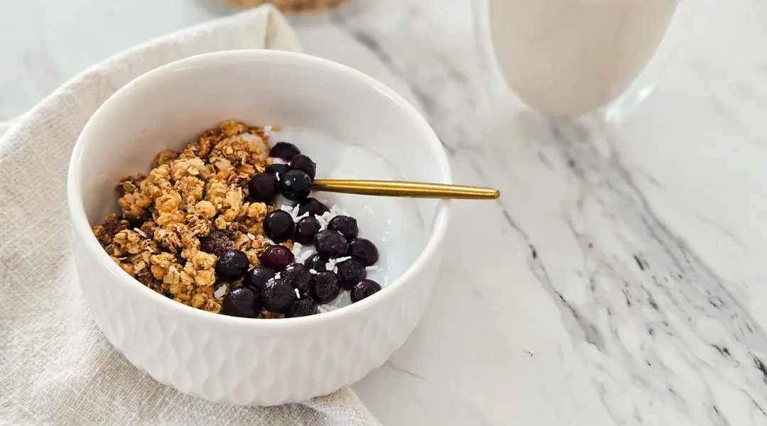 Bol de yogourt garni de granola croustillant, de bleuets et de noix de coco, avec une cuillère dorée