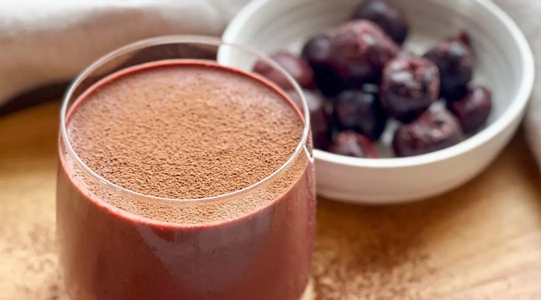 Smoothie épais à la cerise et au cacao dans un verre, avec des cerises surgelées en arrière-plan