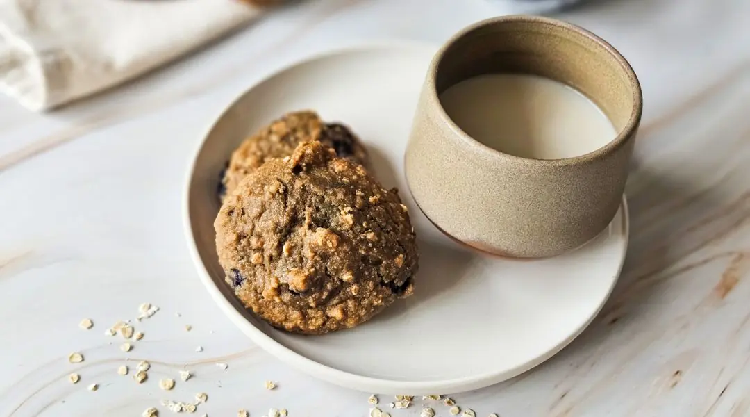 Biscuits à l’avoine et aux bleuets accompagnés d’une tasse de lait végétal sur une assiette beige