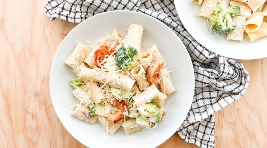 Rigatoni à la sauce Alfredo crémeuse avec crevettes et brocoli, garni de Parmesan dans une assiette blanche