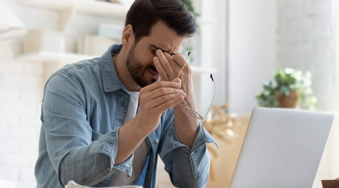 a person sitting in front of a laptop with their hand on their face