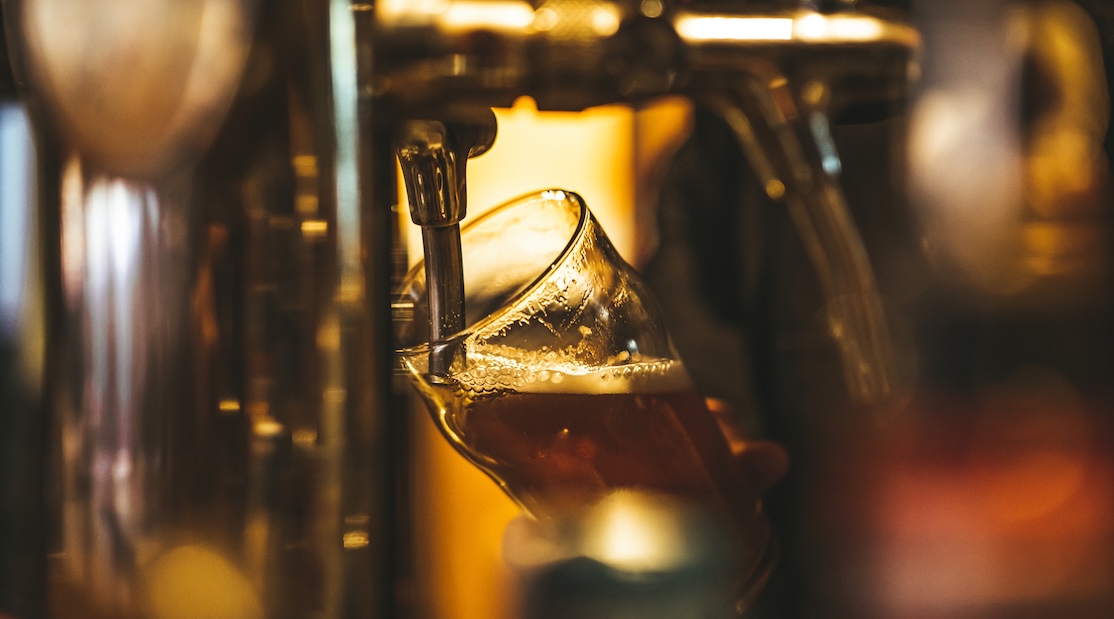 Un verre de bière en train d’être rempli à partir d’une tireuse à bière, avec une lumière dorée en arrière-plan.