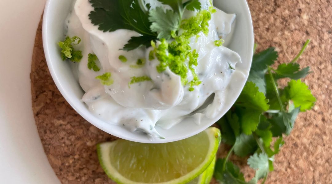 Petit bol de sauce à la coriandre et citron vert avec une tranche de lime et des feuilles de coriandre fraîche sur un tapis en liège