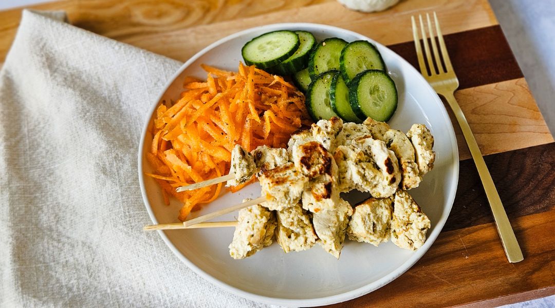 Assiette de brochettes de tofu grillé avec tranches de concombre et carottes râpées, accompagnée d'une fourchette dorée