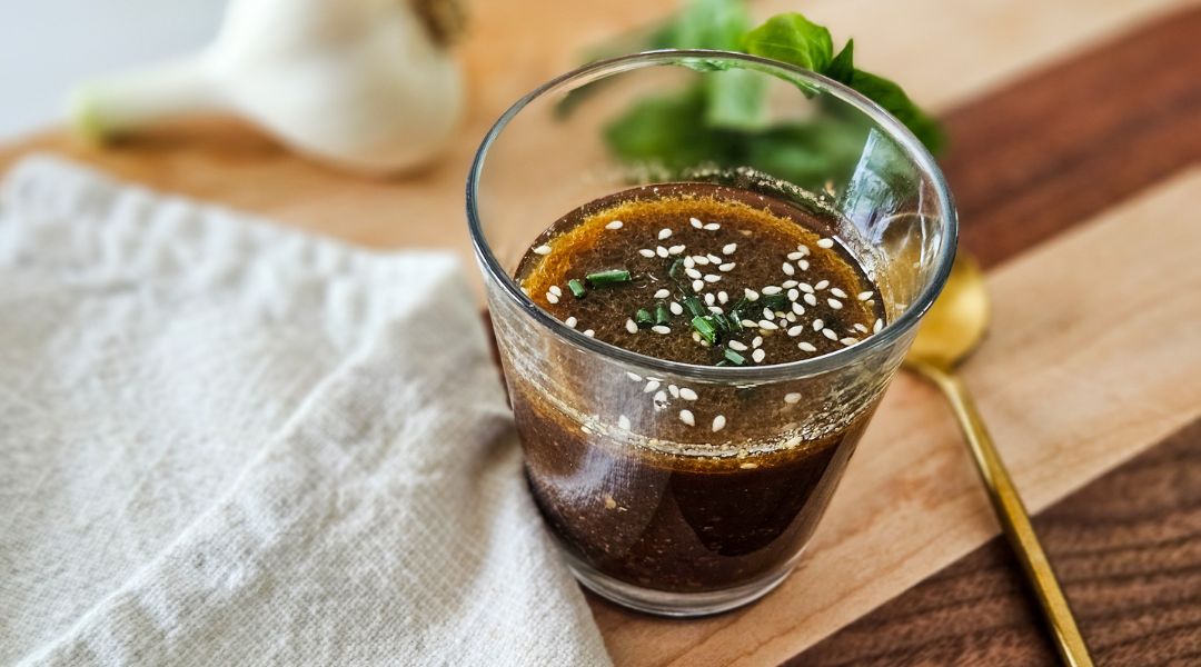 Verre de vinaigrette au miso et gingembre avec graines de sésame et ciboulette, posé sur une planche en bois