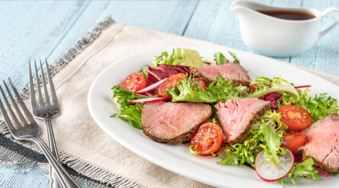 Salade fraîche avec des tranches de filet de bœuf, des feuilles de salade, des tomates cerises et des radis, accompagnée d'une vinaigrette.