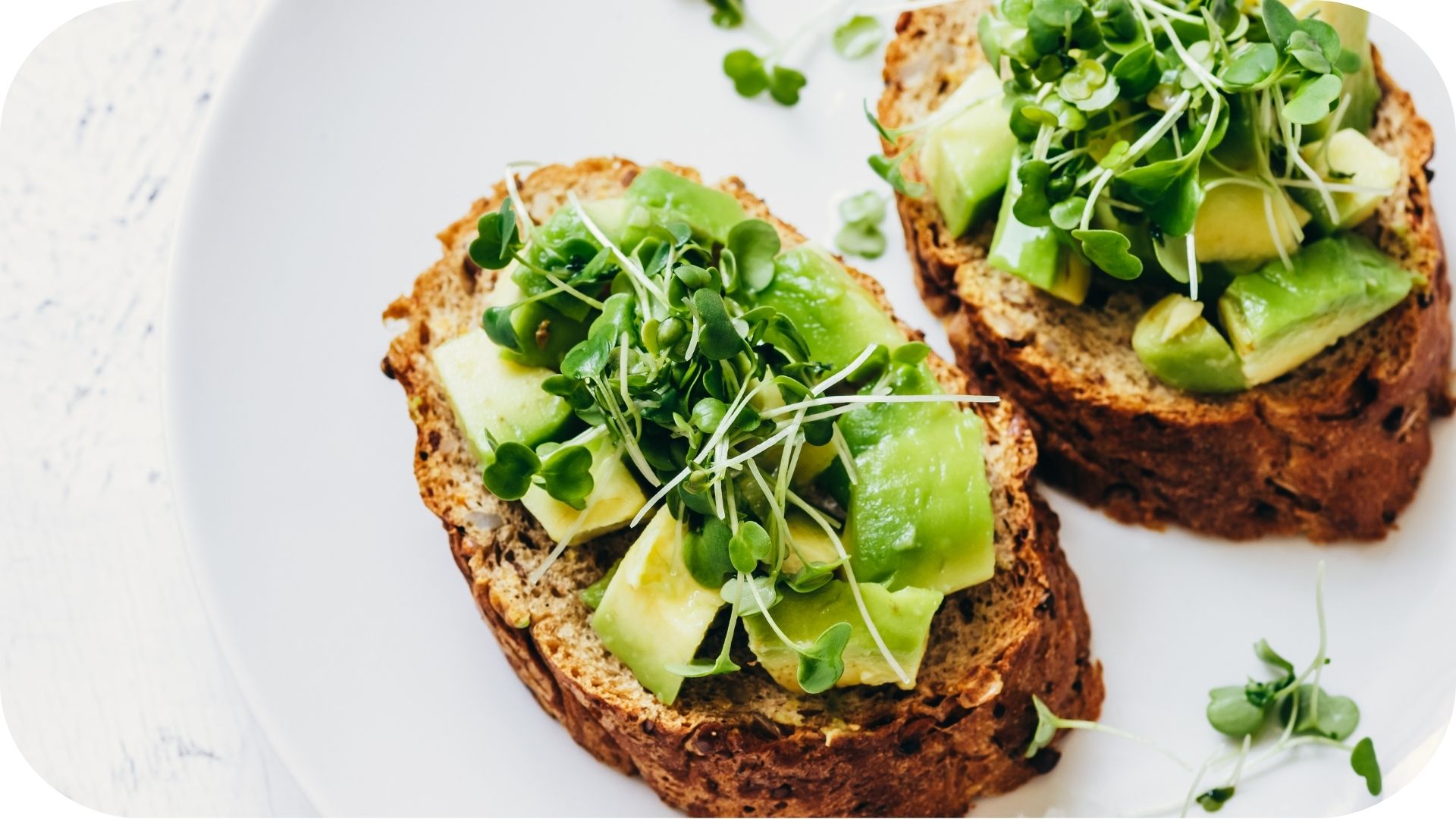 Tranches de pain complet garnies de morceaux d'avocat et de jeunes pousses fraîches sur une assiette blanche