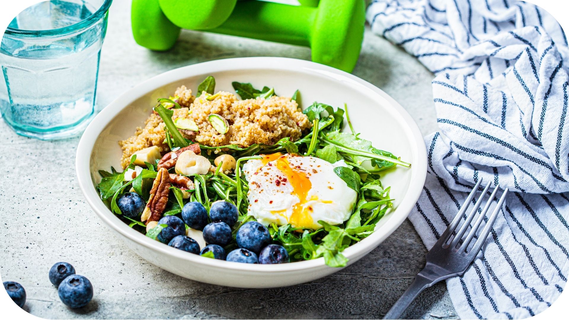 Bol de salade saine avec quinoa, roquette, œuf poché, myrtilles et noix, accompagné d'eau et d'un haltère vert