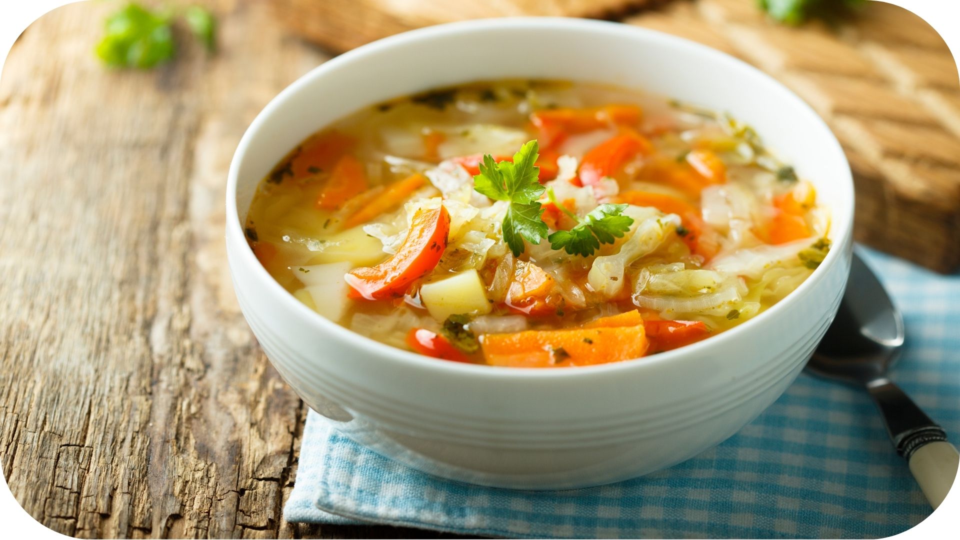 Bol de soupe aux légumes avec carottes, chou et herbes, garni de persil frais sur une table en bois rustique