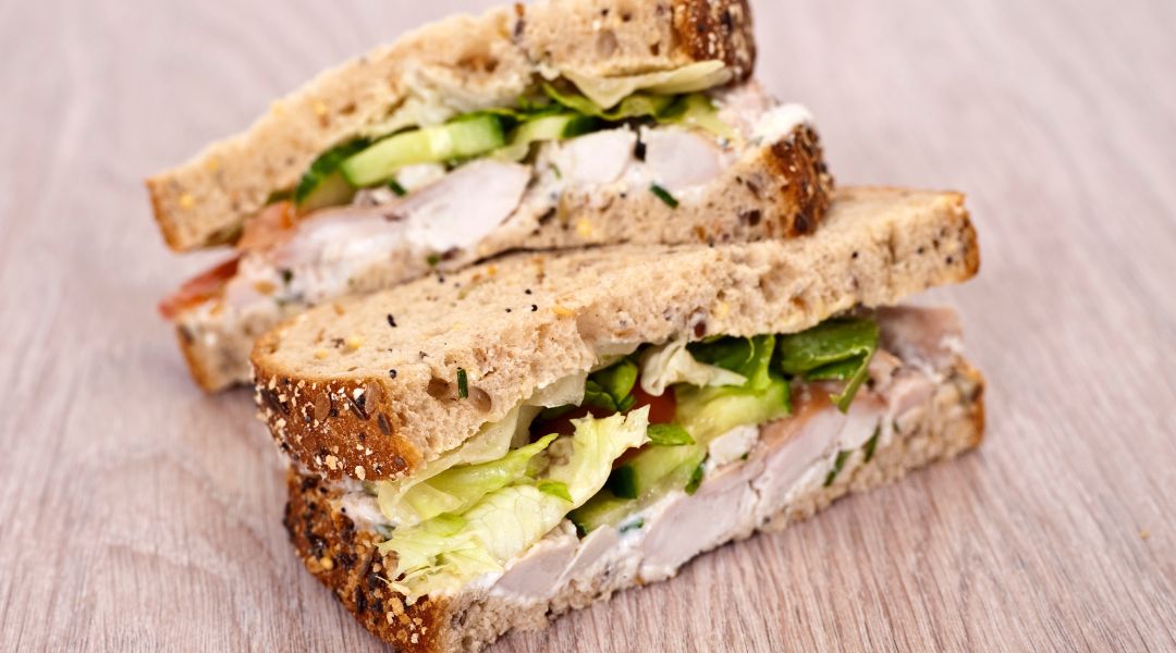 Deux moitiés de sandwich au poulet avec du pain aux céréales, de la laitue, du concombre et une sauce crémeuse, empilées sur une surface en bois.