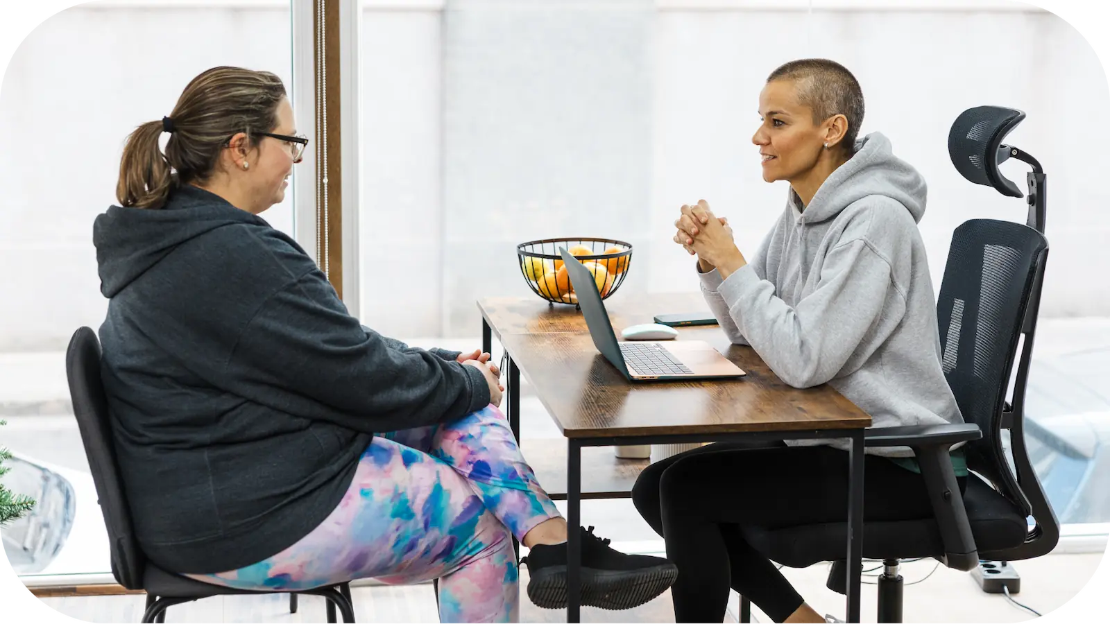 Une nutritionniste discute avec une cliente pendant une consultation en nutrition, assises face à face à une table avec un ordinateur portable et un bol de fruits