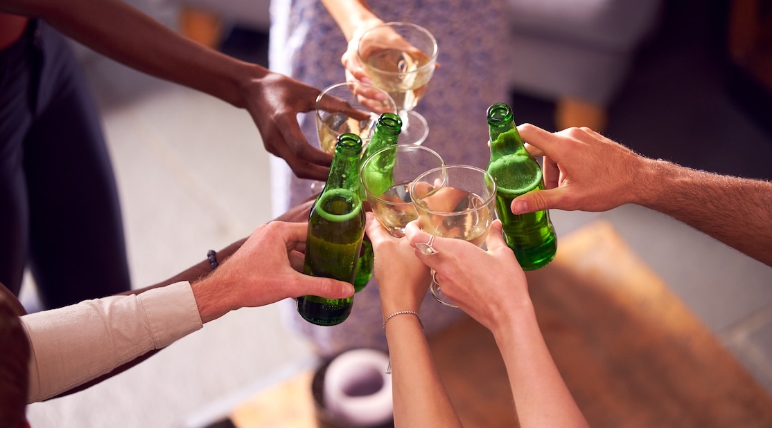 Un groupe de mains diverses trinquant avec des bouteilles de bière verte et des verres de vin dans une ambiance festive.