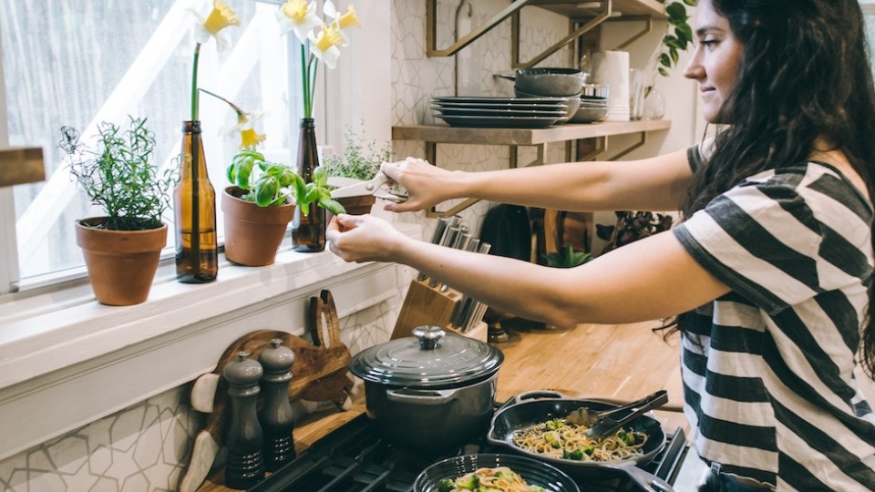 femme dans une cuisine cuisinant un plat et ajoutant du basilic