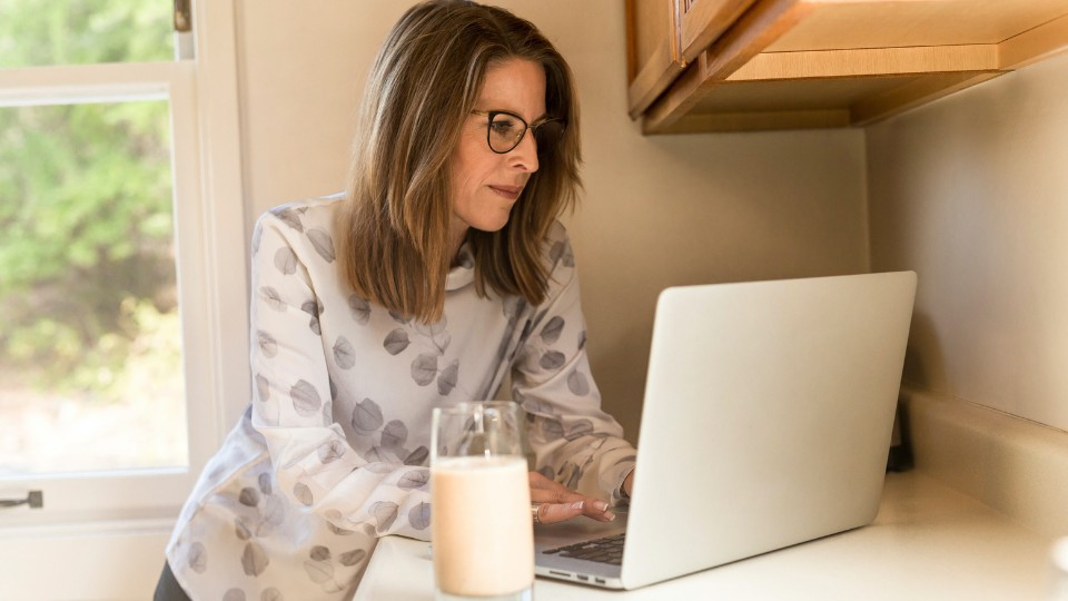 femme ménopausé devant un ordinateur avec un verre de lait