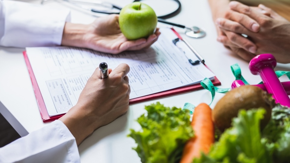 Nutritionniste-diététiste à Toronto qui fait une consultation en nutrition avec un client en tenant une pomme et en prenant des notes.