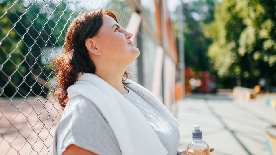 Woman taking a break after outdoor exercise, holding a water bottle, symbolizing a weight loss journey