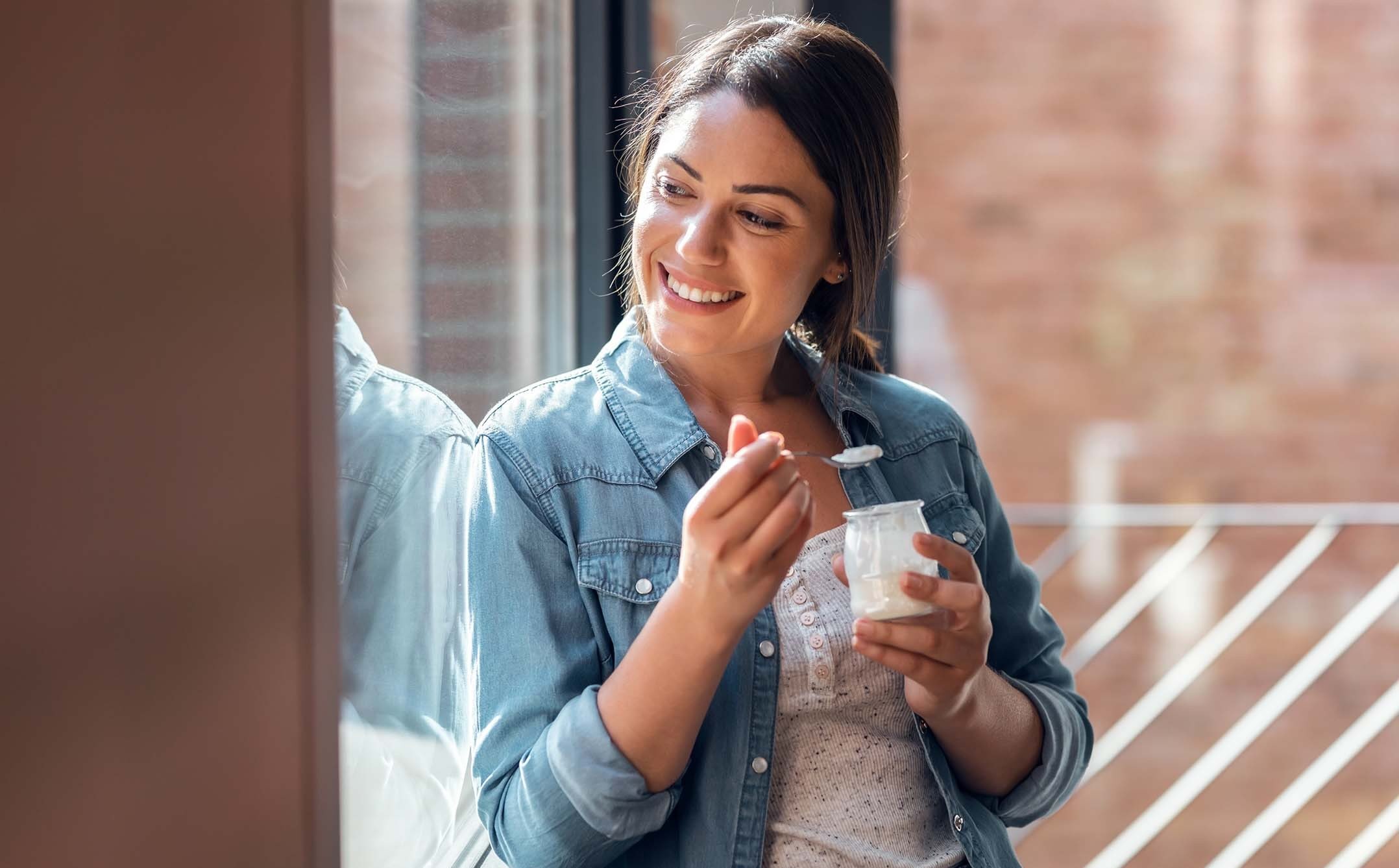 Une femme souriante mange du yaourt près d'une fenêtre - A smiling woman eating yogurt near a window