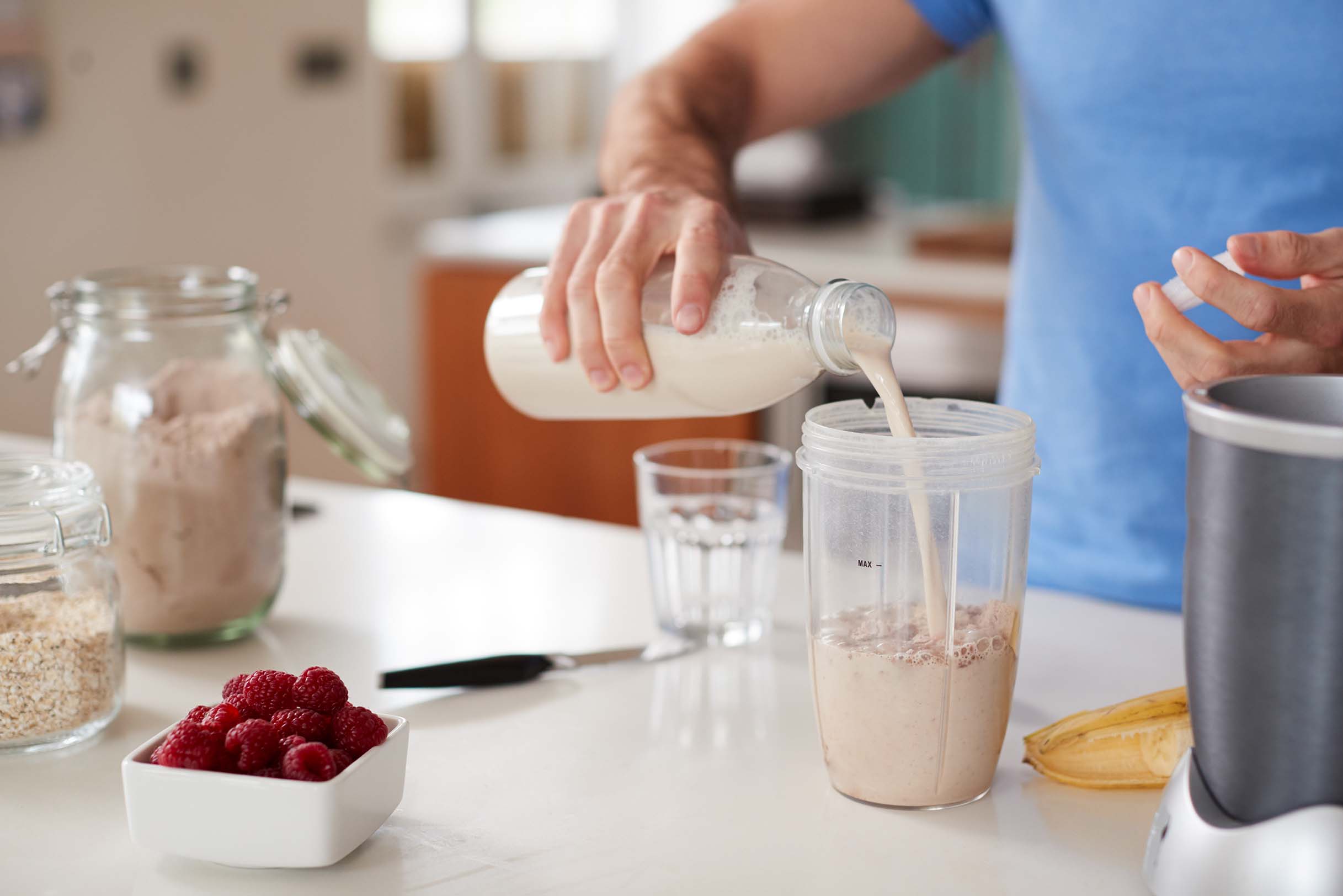 A person in a blue shirt pours a protein shake into a blender cup - Une personne en t-shirt bleu verse un shake de protéines dans un gobelet