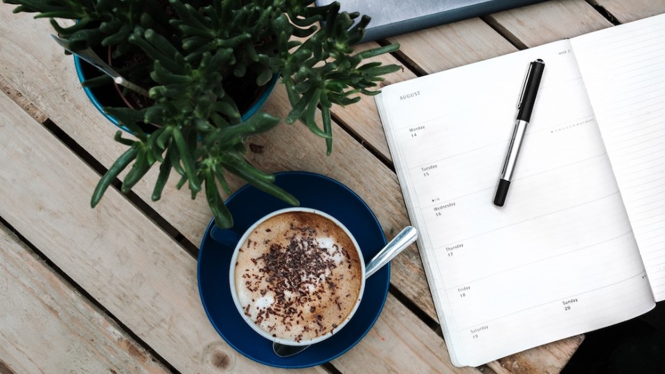 Un agenda, un café et une plante sur une table en bois