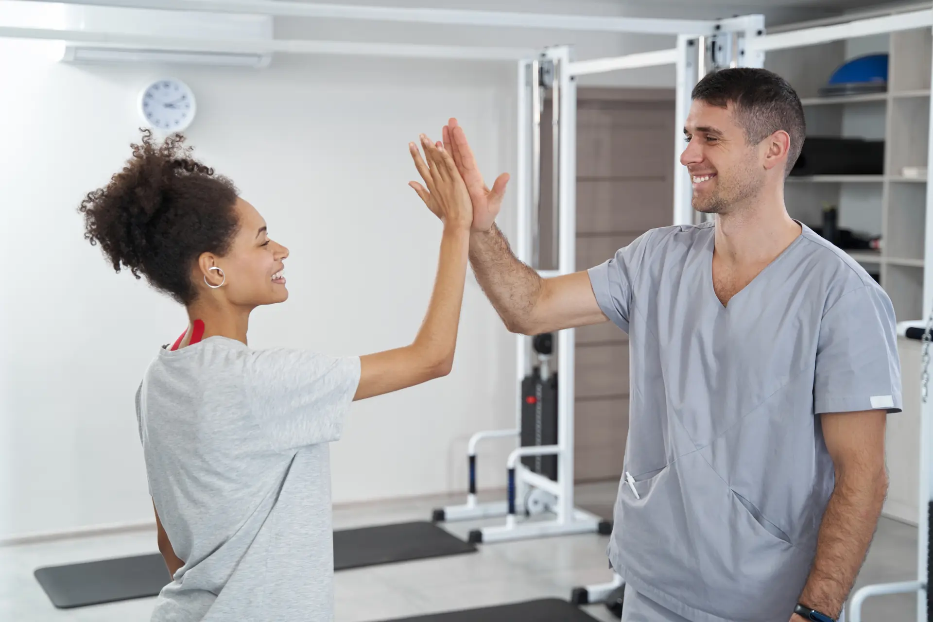 Physiothérapeute sourit et fait un high five avec une jeune femme - A physiotherapist smiles and gives a high five to a young woman