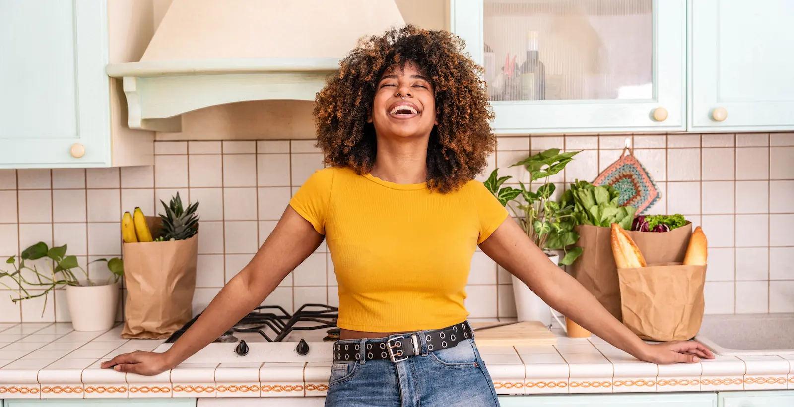 Femme souriante appuyée sur le comptoir de sa cuisine - Smiling woman leaning on her kitchen counter with grocery bags