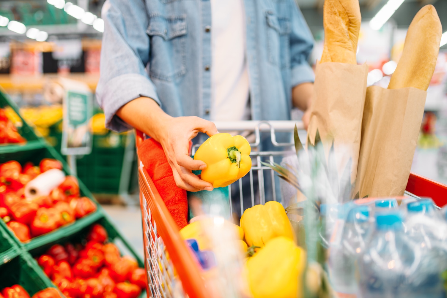A shopper selects a yellow pepper from a display of fresh produce at the grocery store.