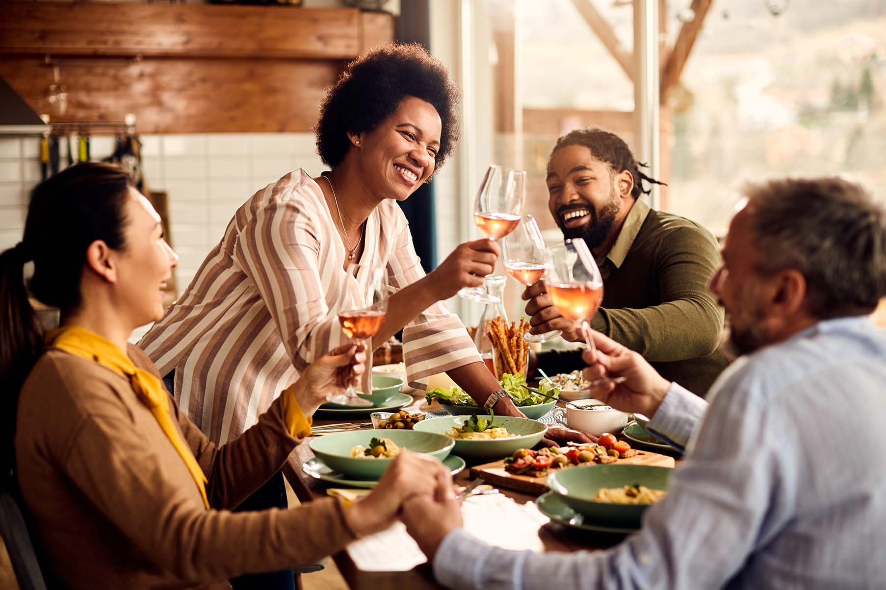 Groupe d'amis multiculturels trinquant avec des verres de vin rosé autour d'un repas - Multicultural group of friends toasting with glasses of rosé wine around a meal