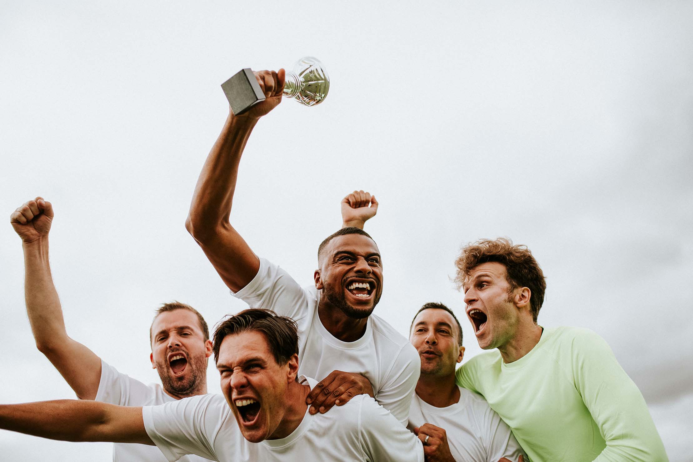 Group of excited men in white jerseys celebrating victory as one holds up a trophy - Groupe d'hommes enthousiastes en maillots blancs célébrant leur victoire, l'un d'eux brandissant un trophée