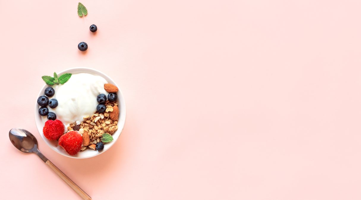 Bol de yogourt garni de granola, bleuets, fraises et amandes sur fond pastel