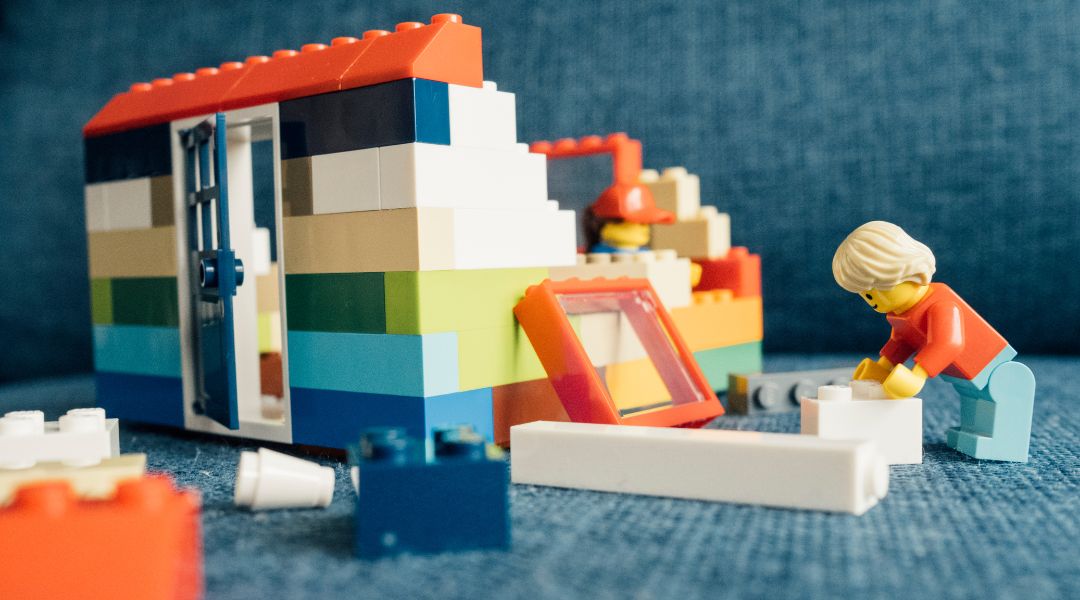 Figurines LEGO construisant une maison en briques colorées avec des pièces éparpillées sur une surface bleue