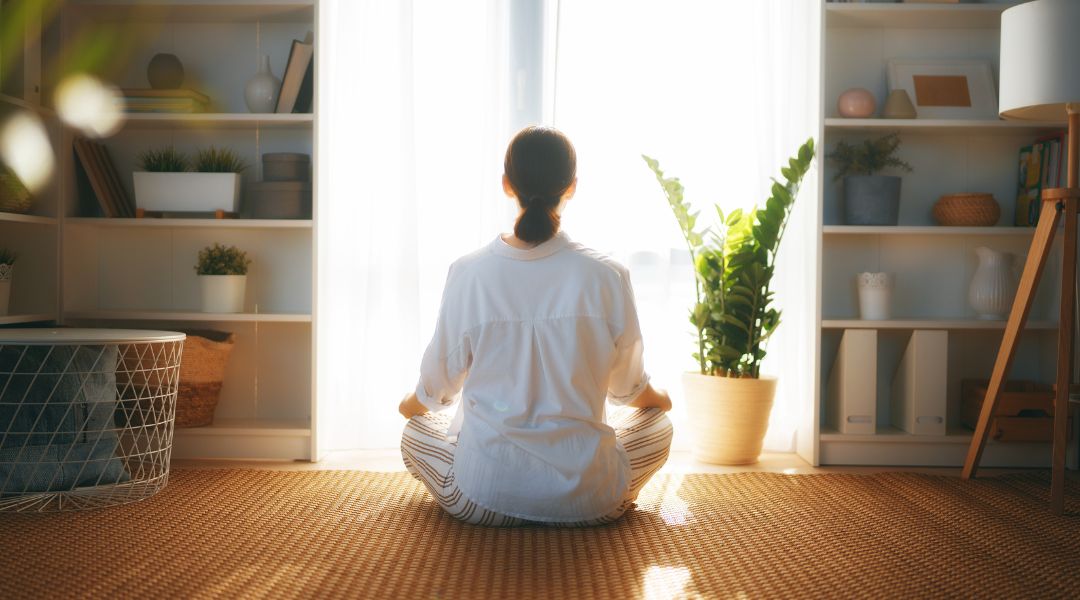 femme qui fait de la méditation dans son salon devant une fenêtre illuminée