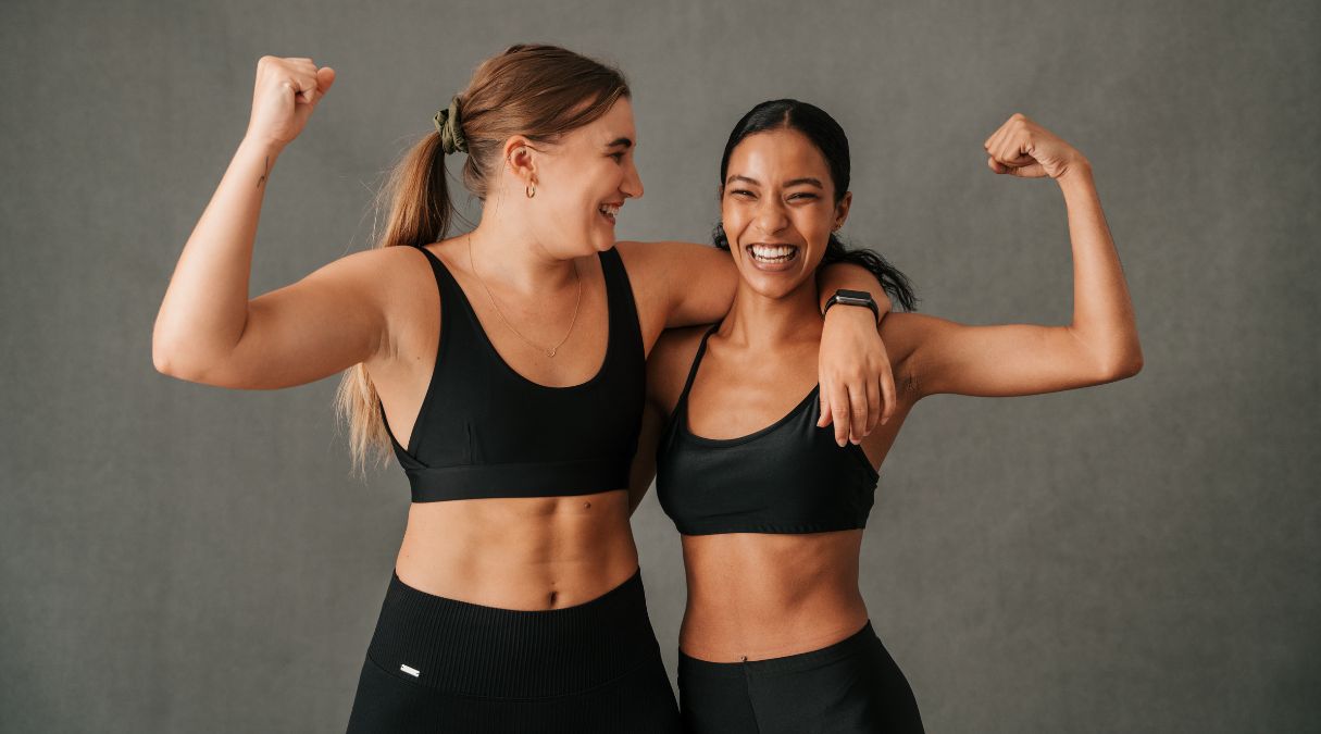 Deux femmes en tenue sportive souriantes, fléchissant leurs bras, célébrant le fitness