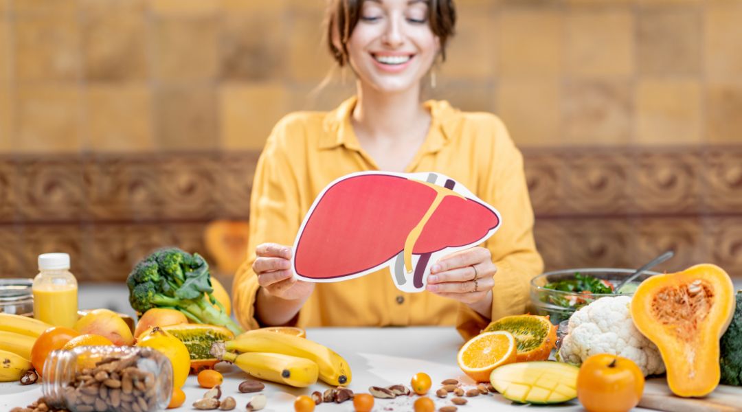 A person holding up a liver surrounded by fruits and vegetables.