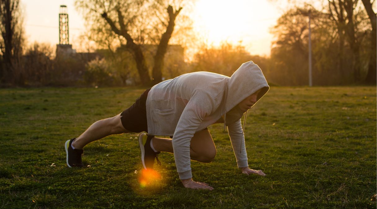 Homme en sweat à capuche faisant des exercices de montagne sur l'herbe au lever du soleil