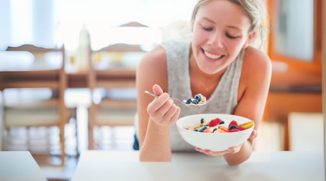 A person is smiling while holding a bowl of fruit and cereal.