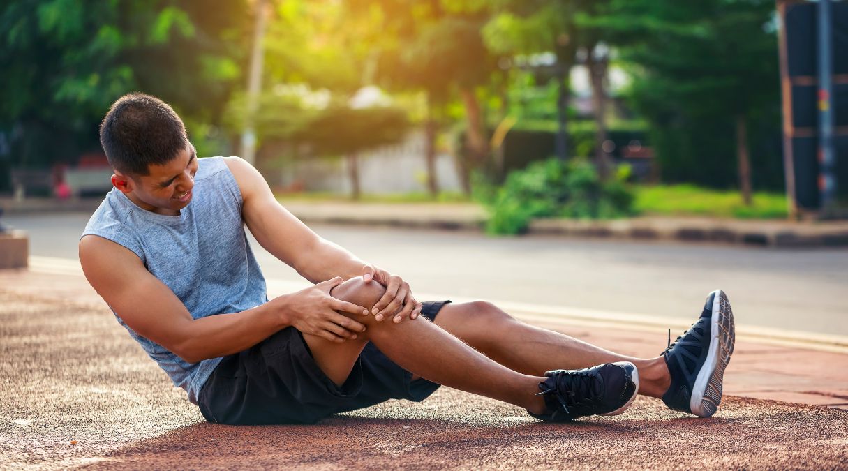 Homme assis au sol tenant son genou, indiquant une blessure sportive possible