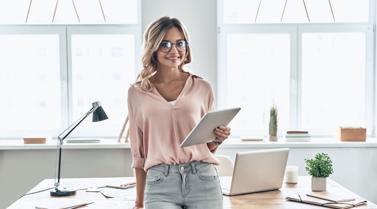 Nutritionniste souriante en blouse rose pâle tenant une tablette dans un bureau lumineux et moderne