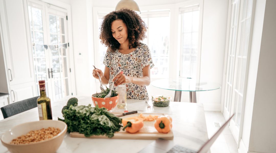 Femme préparant une salade avec des légumes frais dans une cuisine lumineuse, mettant l'accent sur une alimentation saine et simple.