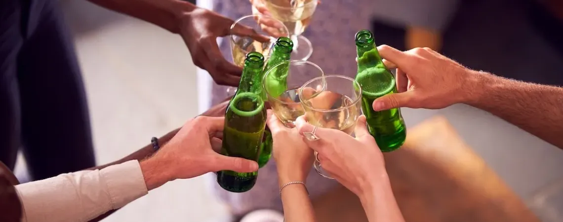Un groupe de mains diverses trinquant avec des bouteilles de bière verte et des verres de vin dans une ambiance festive.