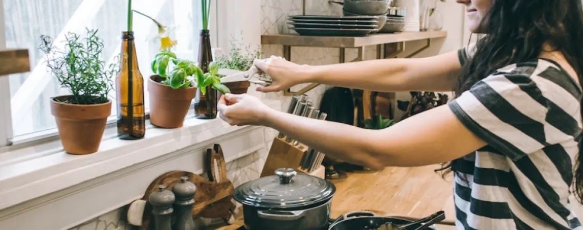 femme dans une cuisine cuisinant un plat et ajoutant du basilic