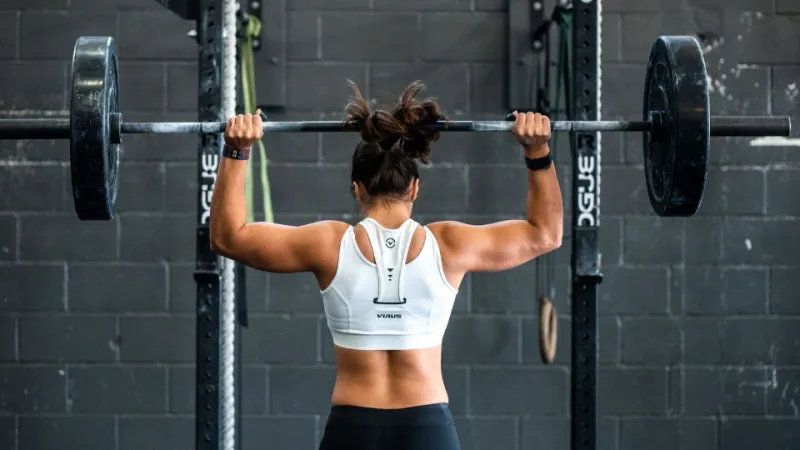 femme de dos musclée qui lève un haltère
