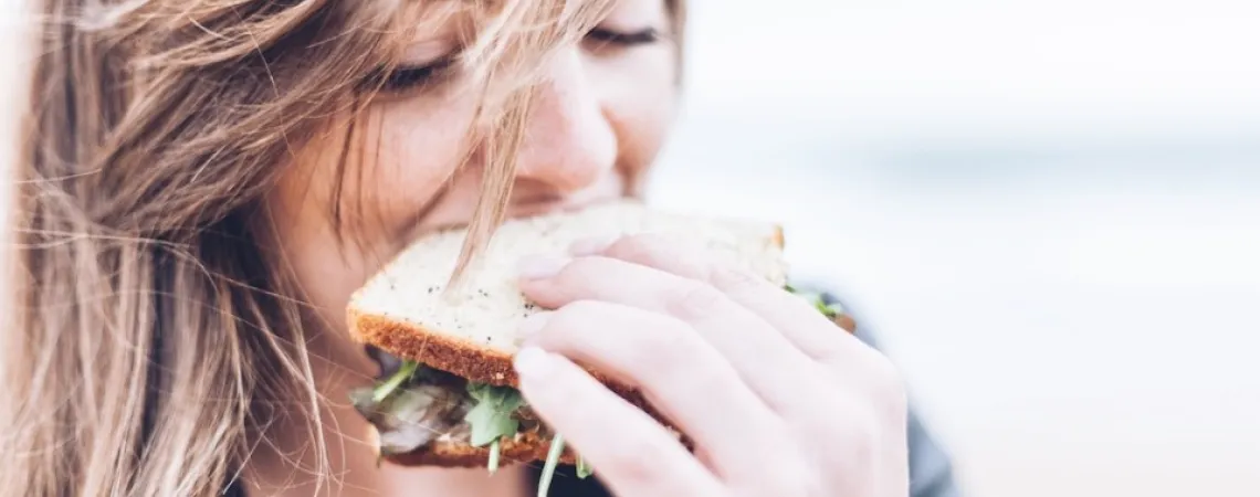 Fille qui mange un sandwich avec du vent dans les cheveux
